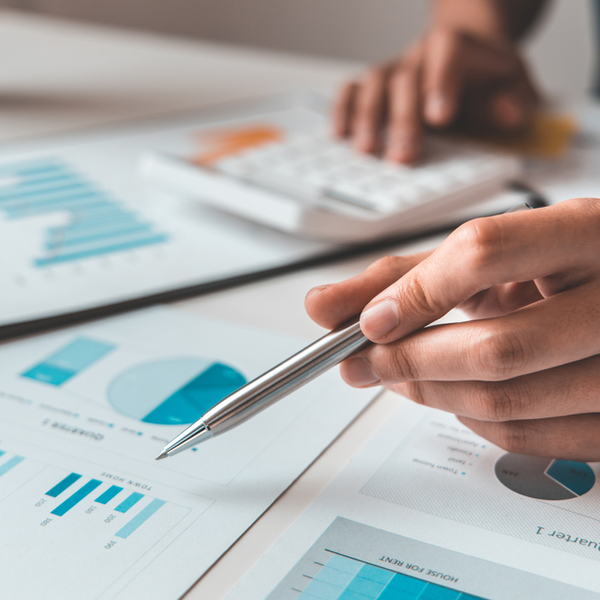 Table filled with paper with graphs and pie charts on as someone uses a calculator