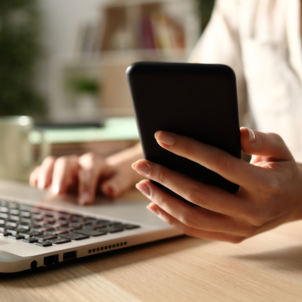 A woman using a laptop while also checking her phone