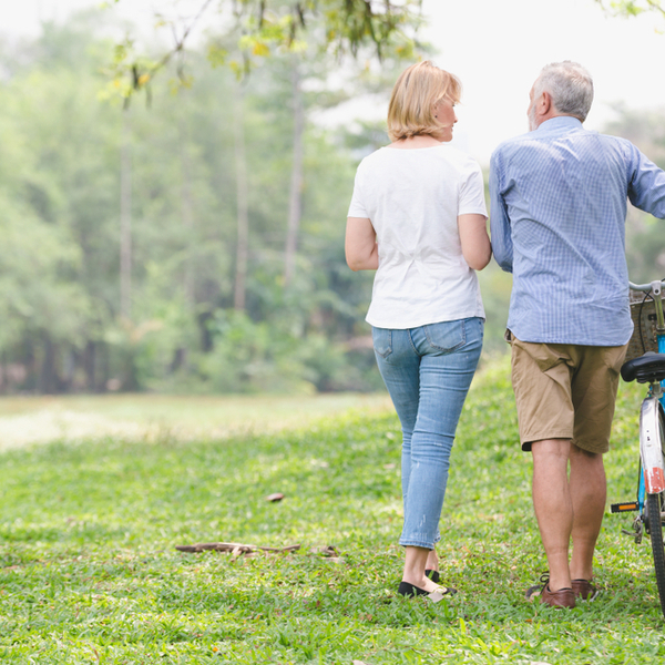 Senior couple walking through the park and pushing a bike