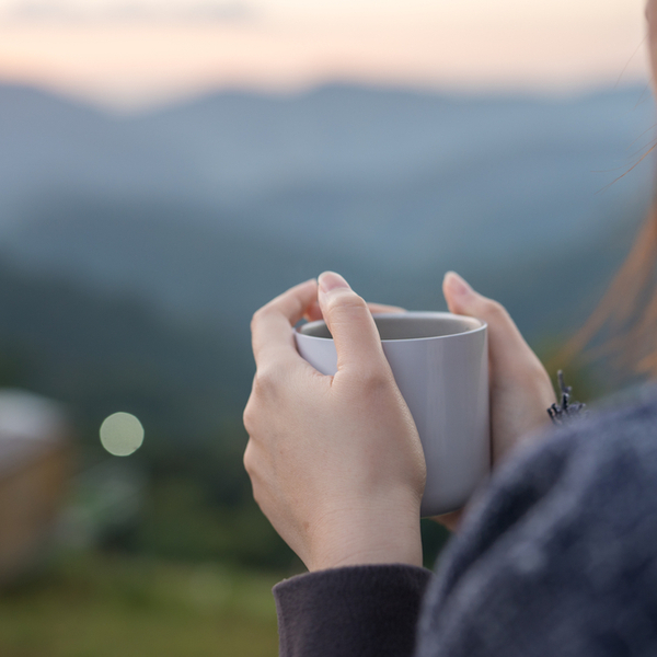 A woman holding a cup of coffee overlooking a green landscape