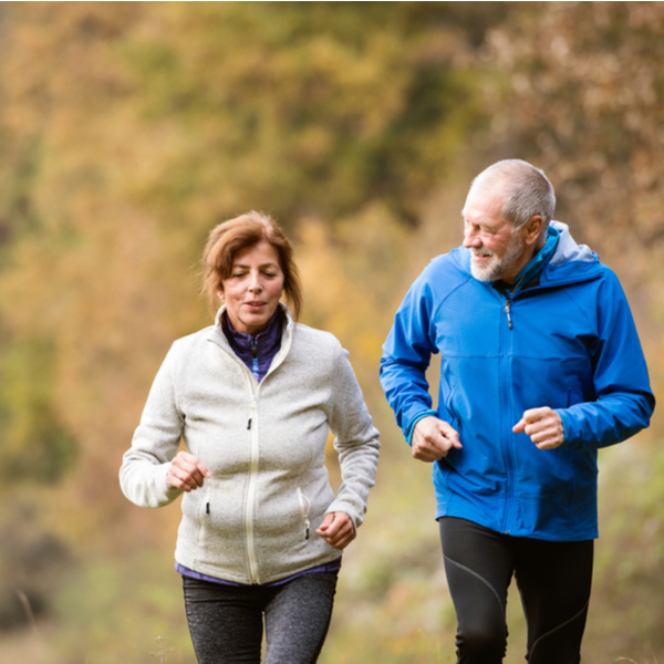 An older couple jogging through a forest in autumn