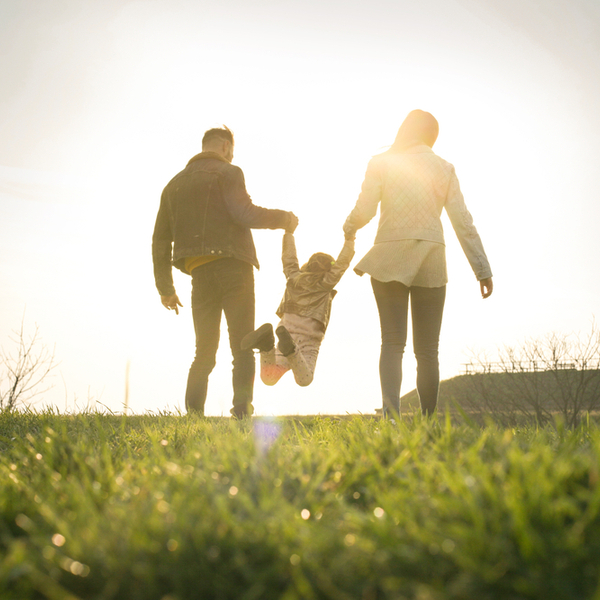 Two parents swinging a child as they walk in the park