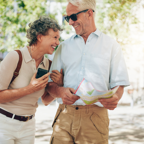 An older couple laughing as they walk around a town with a map