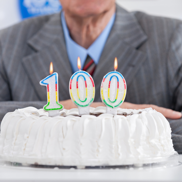 A man sitting behind a cake with “100” birthday candles.