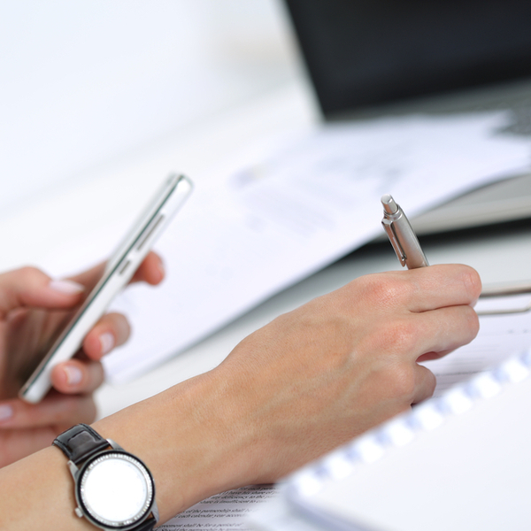 A person taking notes while looking at a phone screen.