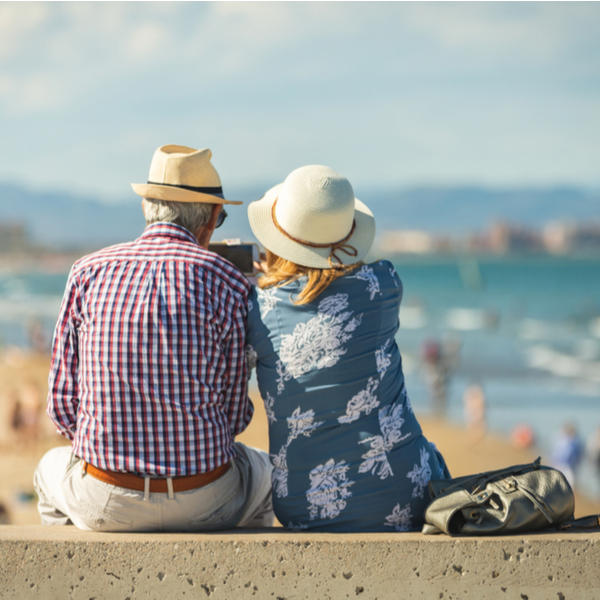 An older couple sitting on a wall at a beach.