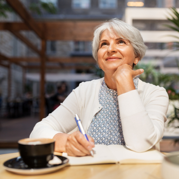 An older woman enjoying a cup of coffee and writing in a journal.