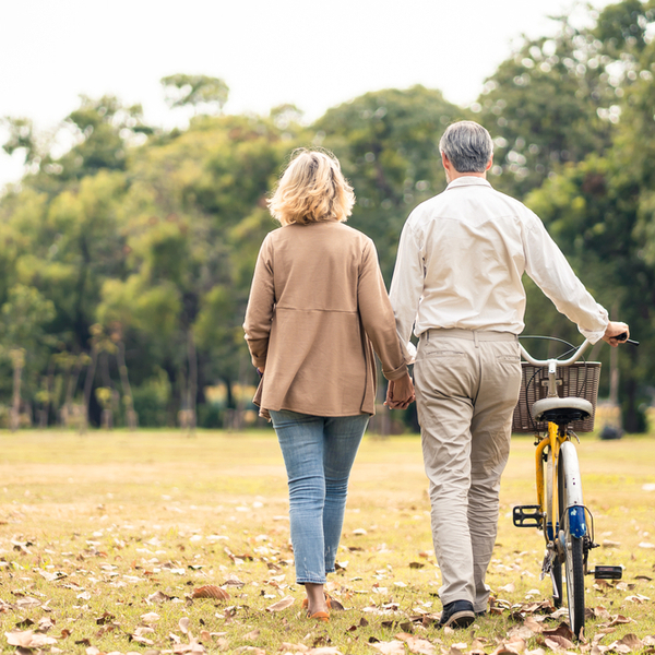 A couple walking through a park and pushing a bike.