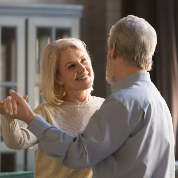 A smiling senior couple dance in their living room