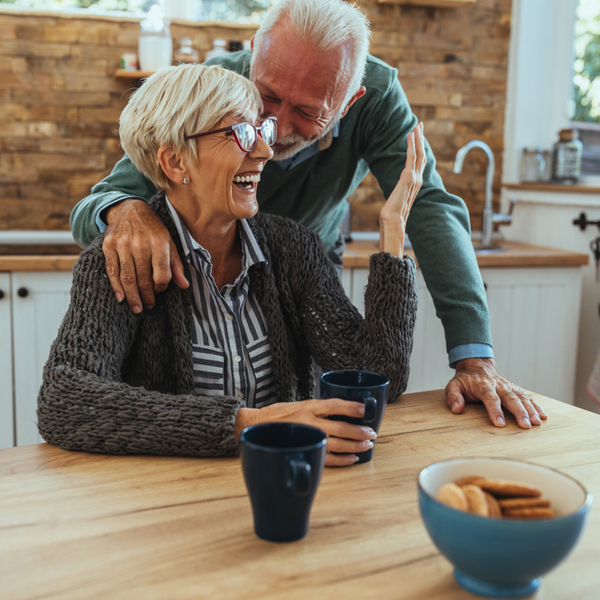 An older couple laughing together in their kitchen.