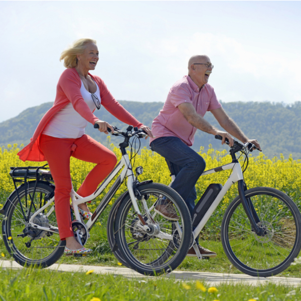 Older couple cycling past a field.