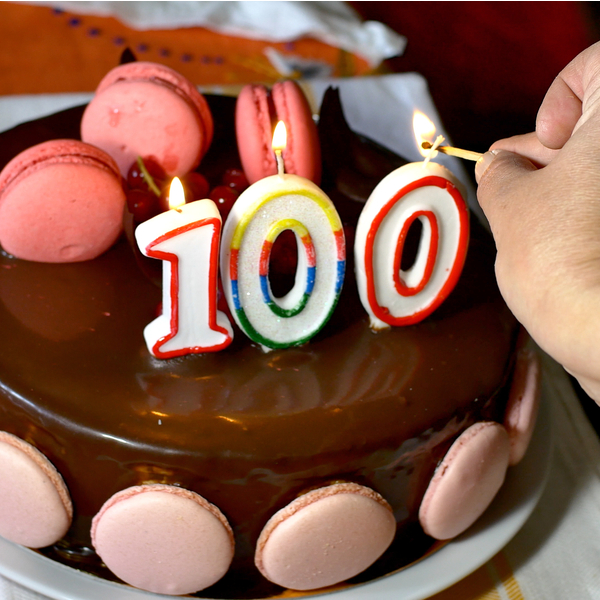 Someone lighting candles on a 100th birthday cake.