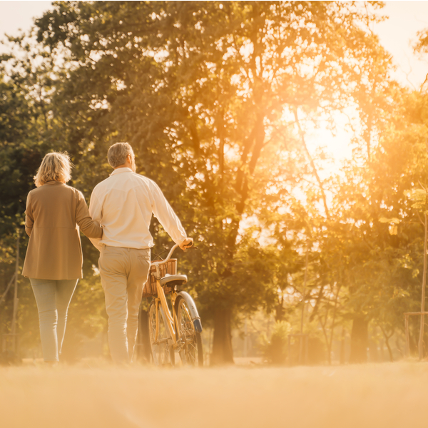A couple walking in a park and pushing a bike.