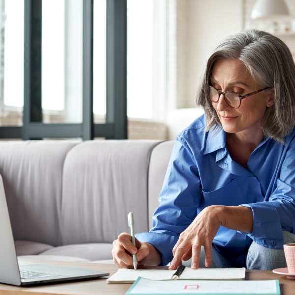 A woman using a laptop and writing notes.
