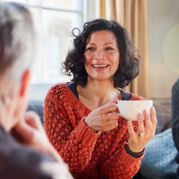 A woman talking to a man while drinking tea.