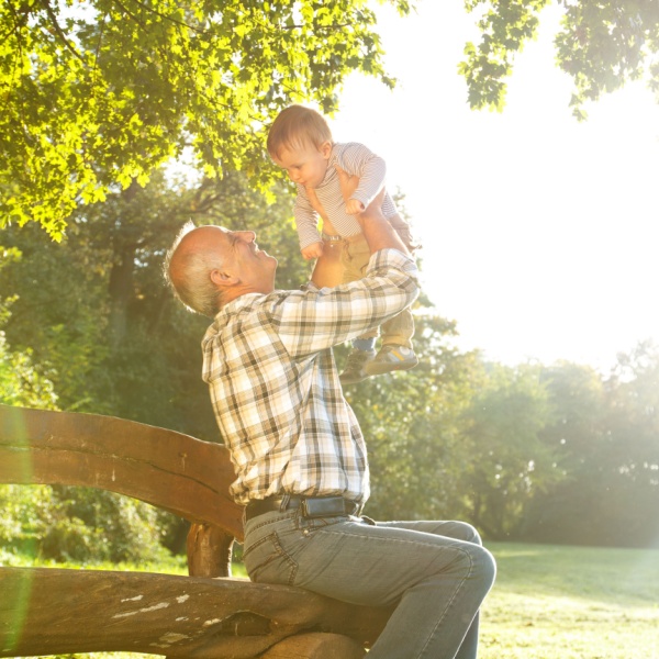 A grandfather playing with his young grandson in a park.