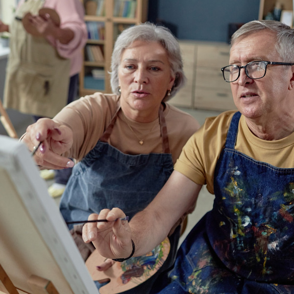 An older couple painting at an easel together.