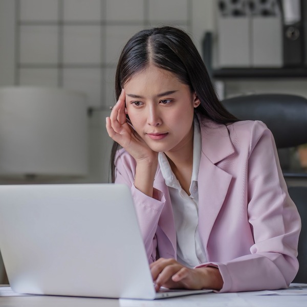 A woman at her computer, thinking carefully.