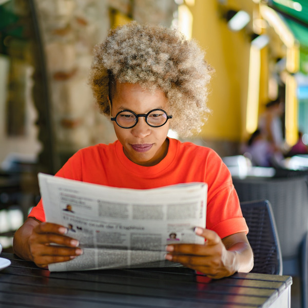 A woman reading a newspaper in a café.